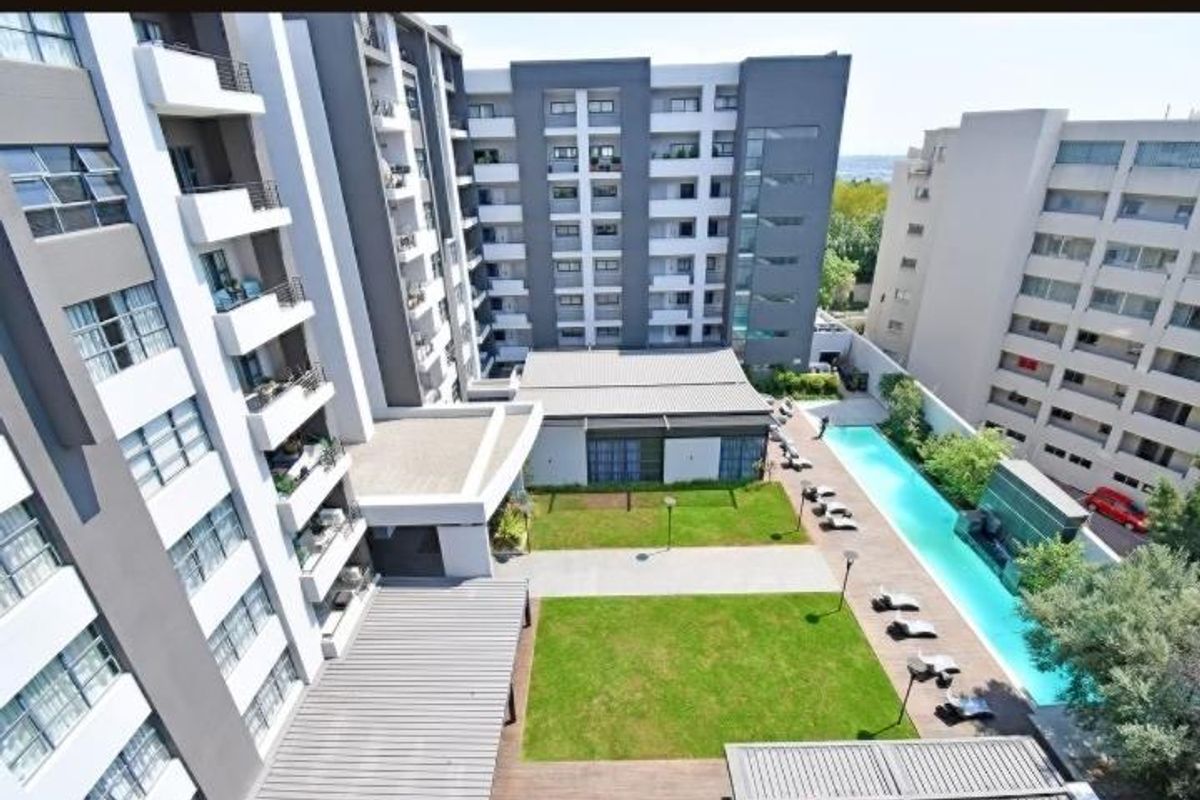 Aerial view of the apartment complex featuring a central landscaped garden, a swimming pool with a deck, and modern building facades.