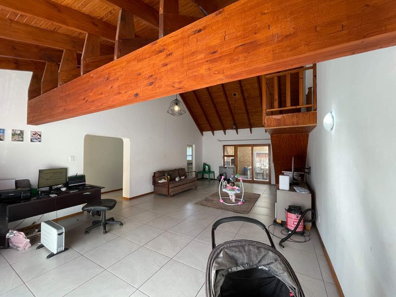 Spacious open-plan living area featuring high vaulted timber ceilings, exposed wooden beams, tiled flooring, and a timber staircase leading to an upper level.