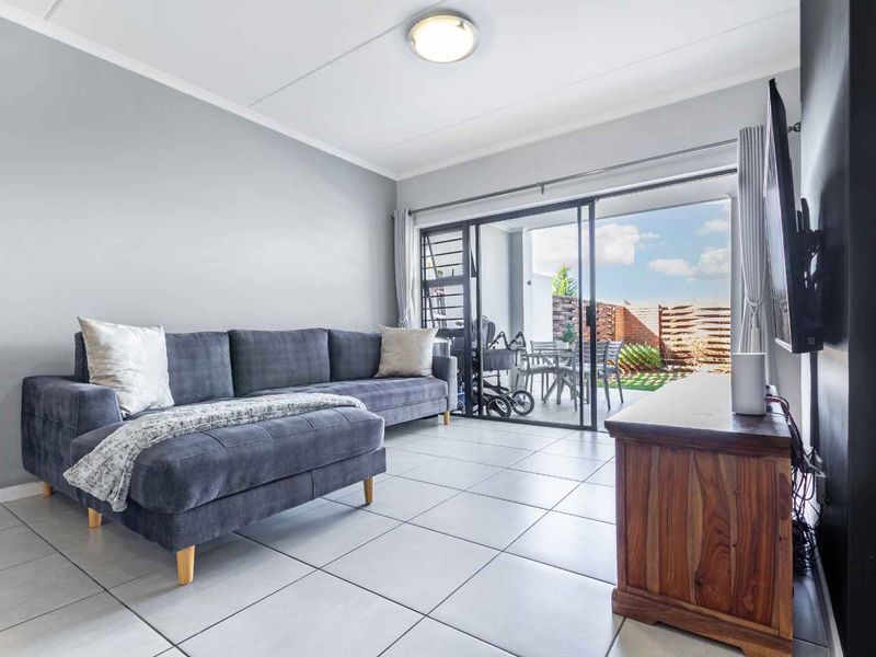 A bright living room featuring neutral tiled flooring and a large sliding glass door providing direct access to an outdoor patio area.