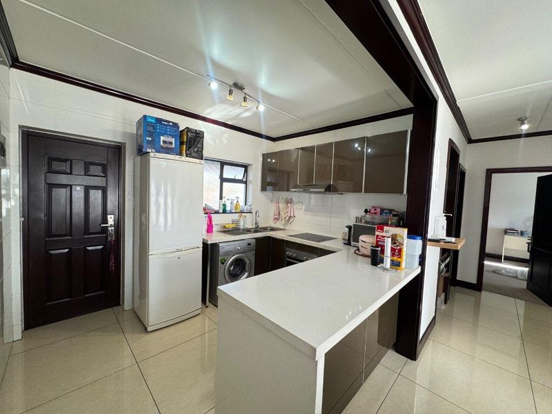 Modern kitchen featuring sleek cabinetry, stone countertops, a breakfast bar, and integrated appliances, seamlessly connected to the living area.