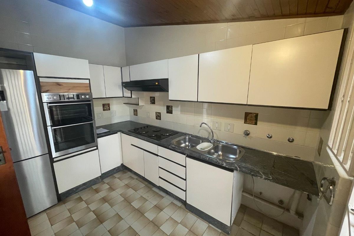 A functional kitchen featuring built-in oven, hob, extractor fan, double sink, and ample cabinetry with a timber ceiling finish.