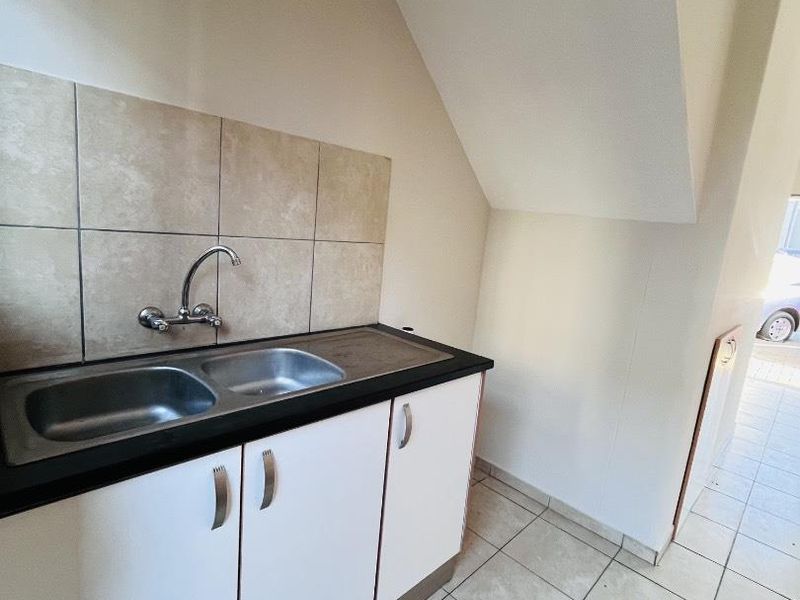 A compact kitchen area featuring a double bowl sink, tiled splashback, and white base cabinetry, situated under a sloped ceiling.