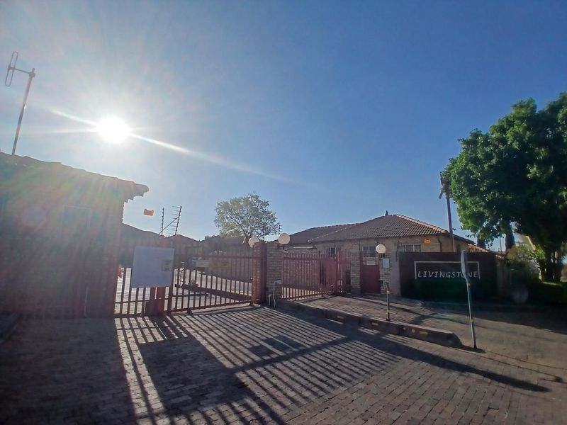 Front entrance view of the Livingstone townhouse complex featuring a secure gated access point, brick paving, and perimeter security fencing.