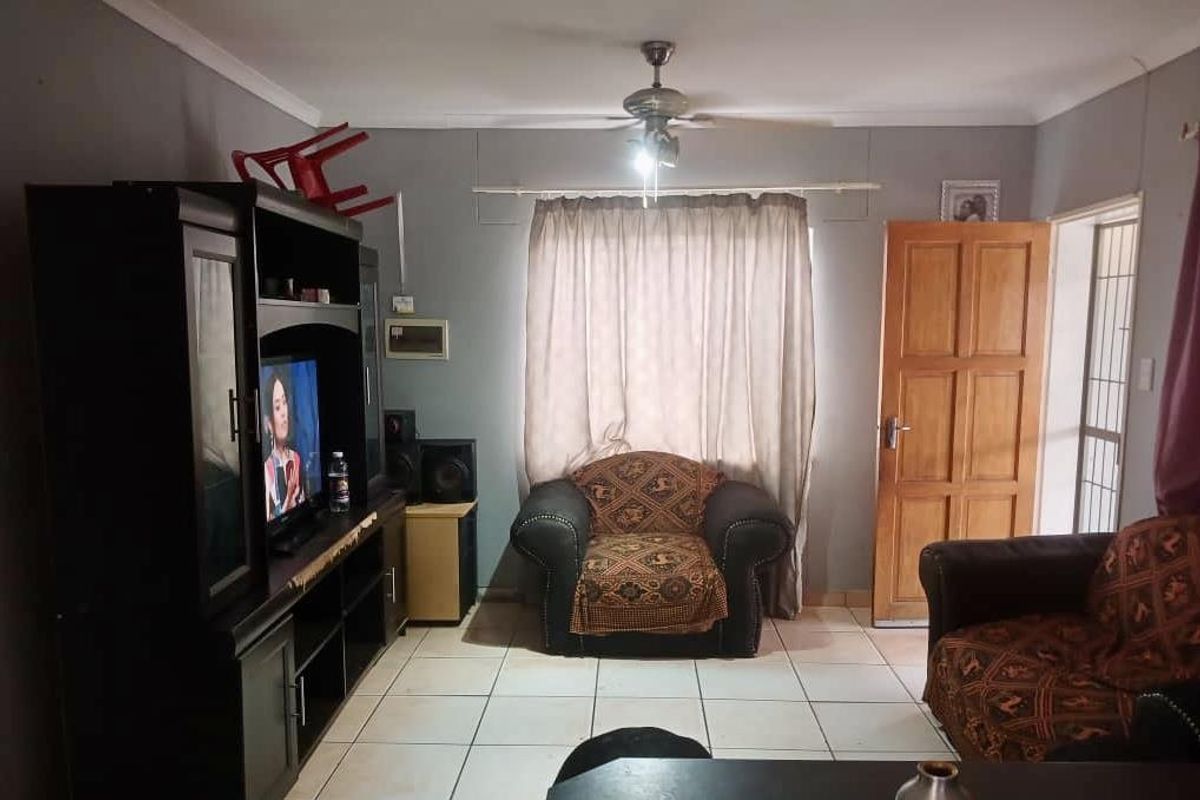 A living room featuring tiled flooring, a ceiling fan, and a wooden door leading to an exterior area.