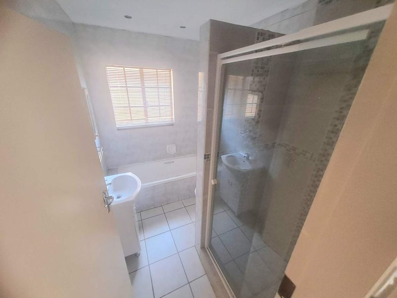 A functional bathroom featuring a bathtub, separate shower enclosure, and pedestal basin with neutral tiled finishes and natural light.