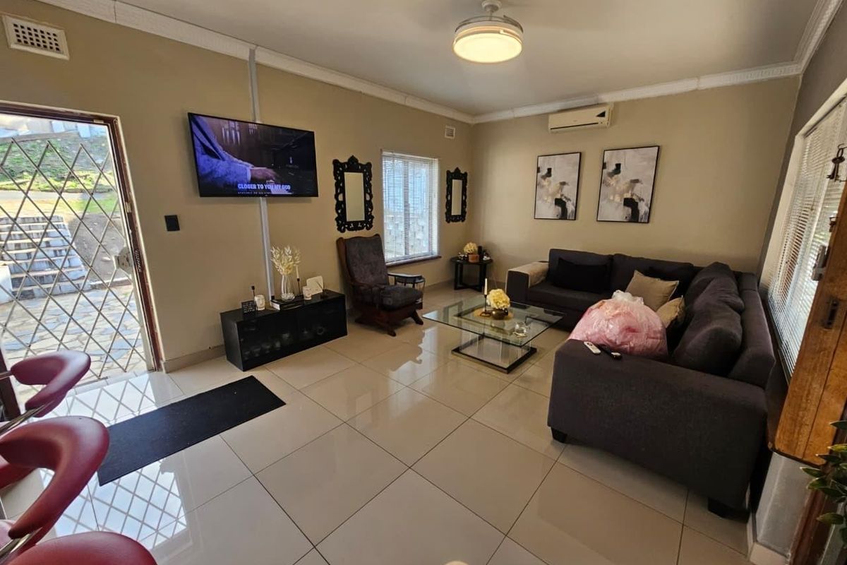 A well-maintained living room featuring large format floor tiles, a split-system air conditioner, ceiling fan, and direct access to an outdoor area via a security gate.