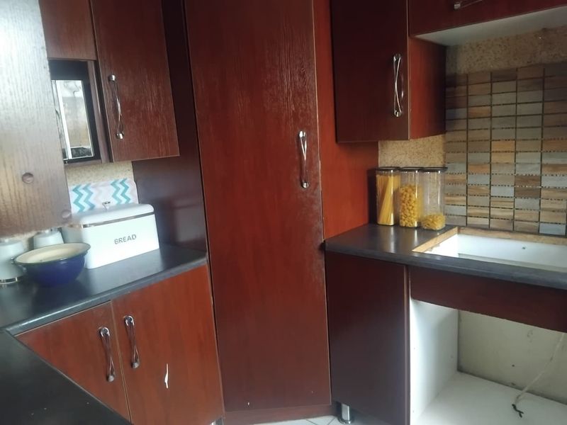 A dated kitchen featuring dark wood-look laminate cabinetry, a mosaic tile backsplash, and dark countertops, showing signs of wear and missing cabinetry components.