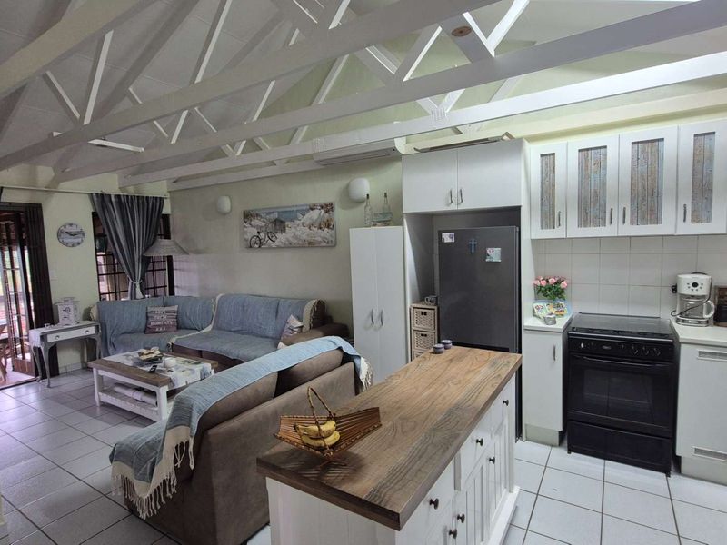 Open-plan living area featuring exposed roof trusses, tiled flooring, and a functional kitchen with a central island and ample cabinetry.