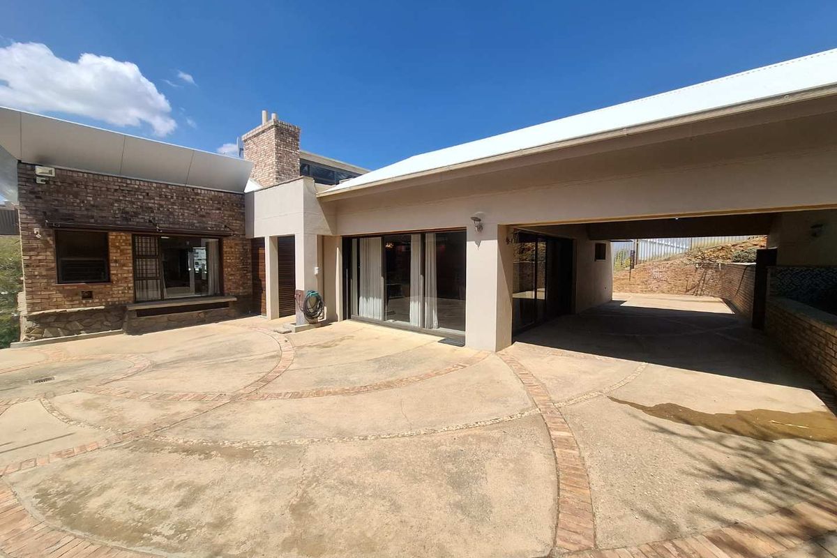 Rear exterior view featuring a paved courtyard, covered patio area, and brick architectural details under a clear blue sky.