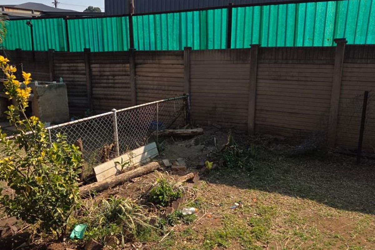 Rear garden area featuring a precast concrete boundary wall with privacy screening, chain link fencing, and a stone paved patio section.