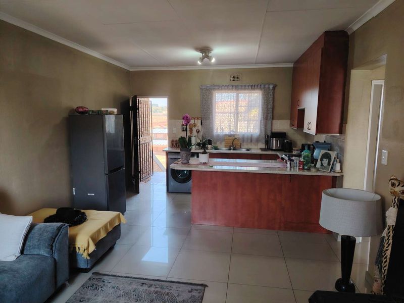 Open plan living area featuring a kitchen with wooden cabinetry, a breakfast bar, and tiled flooring, with direct access to an exterior space.