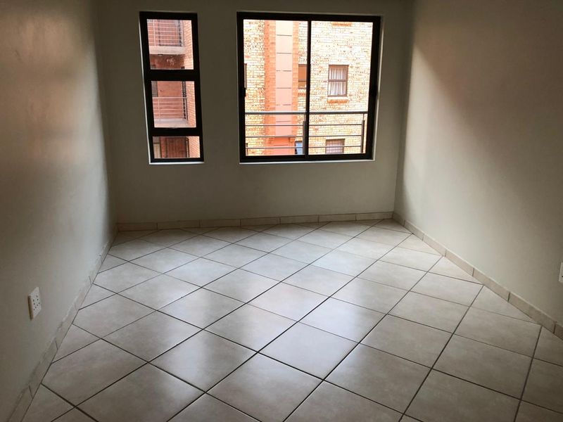 An empty bedroom featuring neutral tiled flooring and aluminium-framed windows, providing a clean and versatile space ready for furnishing.