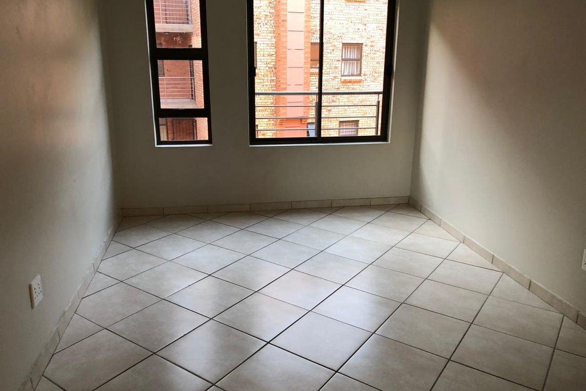 An empty bedroom featuring neutral tiled flooring and aluminium-framed windows, providing a clean and versatile space ready for furnishing.