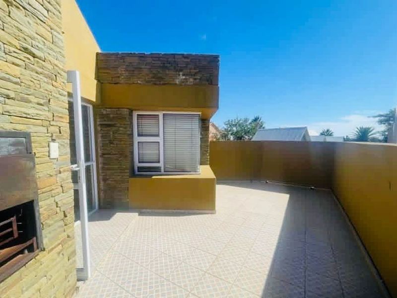 A spacious outdoor balcony featuring stone cladding, tiled flooring, and a built-in braai area, perfect for outdoor entertaining.
