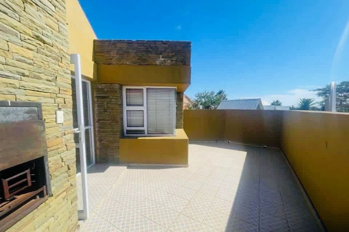 A spacious outdoor balcony featuring stone cladding, tiled flooring, and a built-in braai area, perfect for outdoor entertaining.