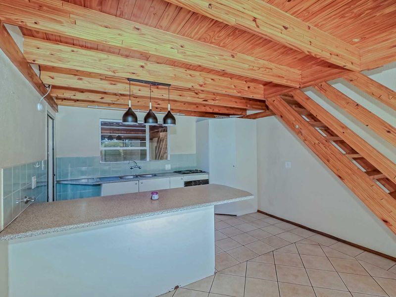 Open-plan kitchen featuring exposed timber ceiling beams, built-in cabinetry, a breakfast bar, and a timber staircase leading to the upper level.