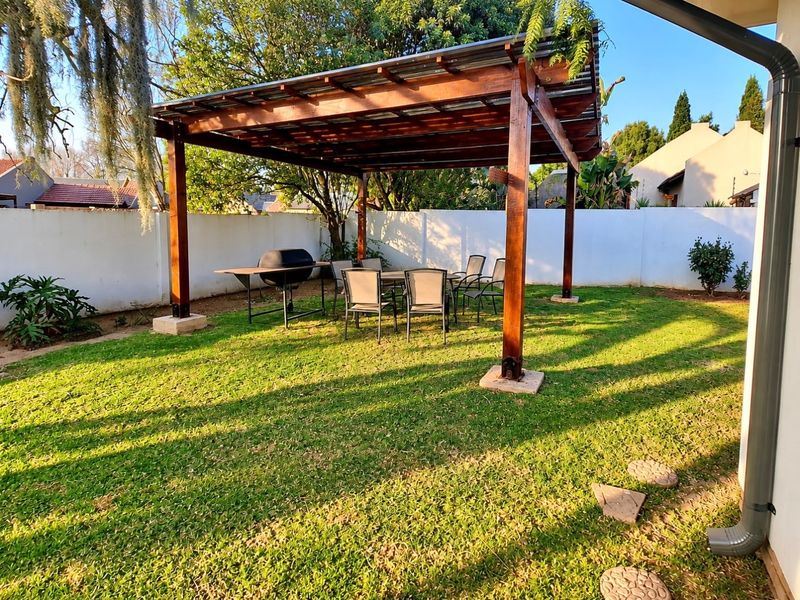 A well-maintained outdoor living space featuring a sturdy timber pergola with a corrugated roof, set within a private, walled garden area.