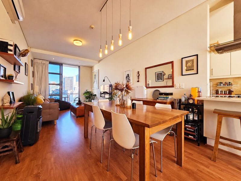 An open-plan living and dining area featuring laminate flooring, modern pendant lighting, and a functional kitchen with built-in cabinetry and an extractor fan.