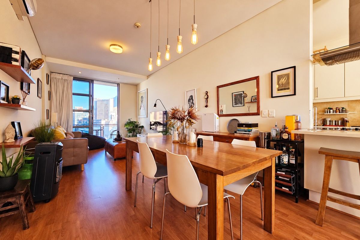 An open-plan living and dining area featuring laminate flooring, modern pendant lighting, and a functional kitchen with built-in cabinetry and an extractor fan.