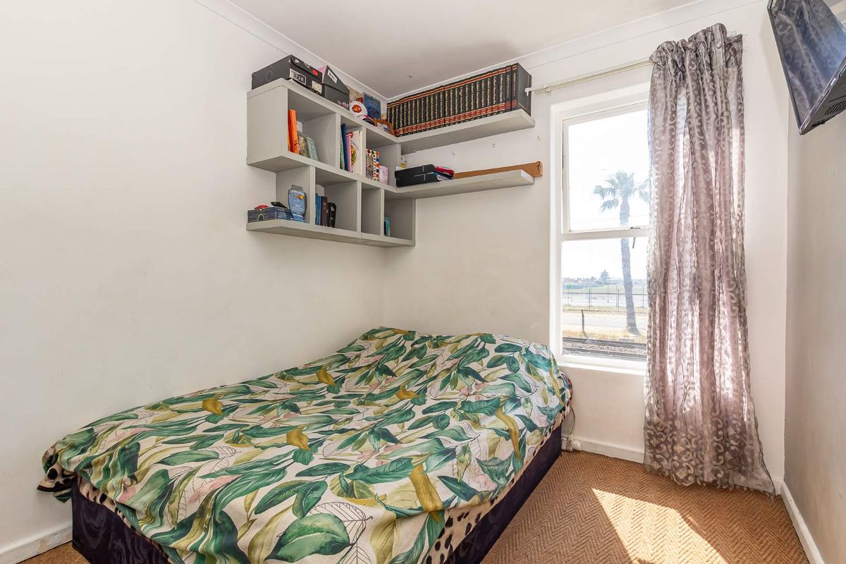 A compact bedroom featuring built-in corner shelving, a window with natural light, and neutral wall finishes.