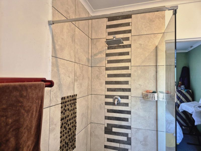 A shower enclosure featuring modern tiled walls with a decorative mosaic accent strip, a fixed glass screen, and a square rainfall shower head.