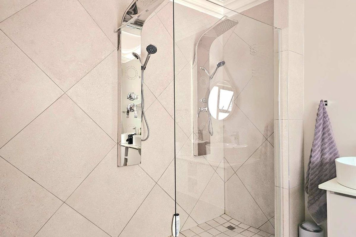 Modern walk-in shower featuring dual stainless steel shower panels with integrated rainfall and handheld showerheads, finished with neutral diamond-patterned wall tiling.