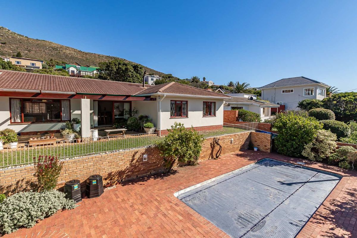Rear exterior view featuring a paved pool area with a pool cover, a brick retaining wall, and a covered patio attached to the house.