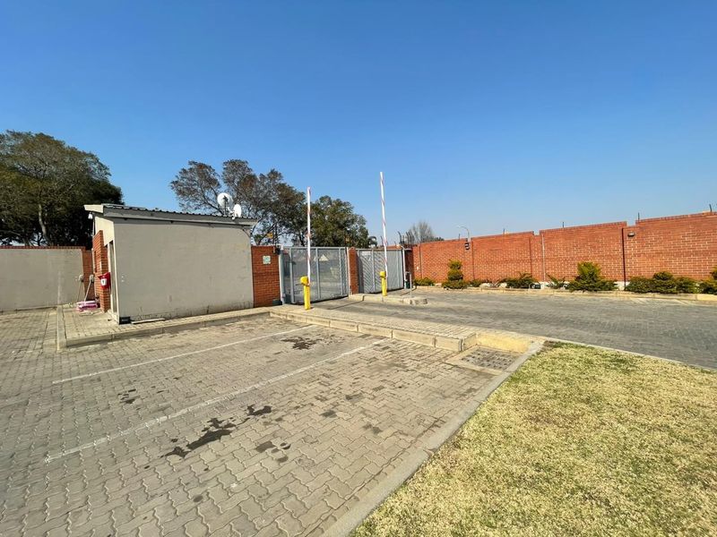 Secure apartment complex entrance featuring a paved driveway, automated boom gates, security fencing, and a dedicated guard house.