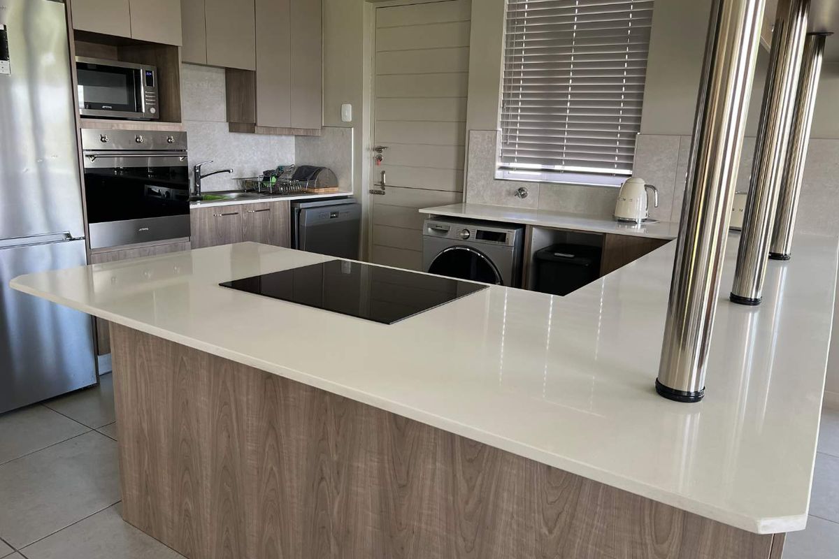 Modern open-plan kitchen featuring stone countertops, integrated hob, built-in oven, microwave, and sleek cabinetry with neutral finishes.