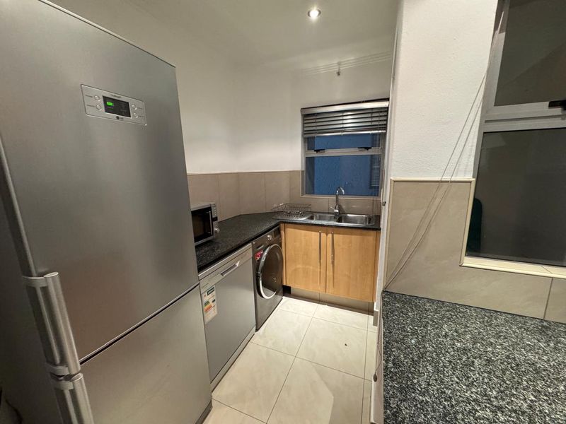 A functional kitchen featuring granite countertops, double basin sink, tiled splashbacks, and ample built-in cabinetry with tiled flooring.