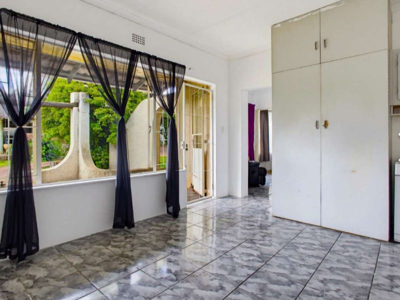 An empty living area featuring tiled flooring, built-in storage cupboards, and large windows providing natural light and access to the exterior.