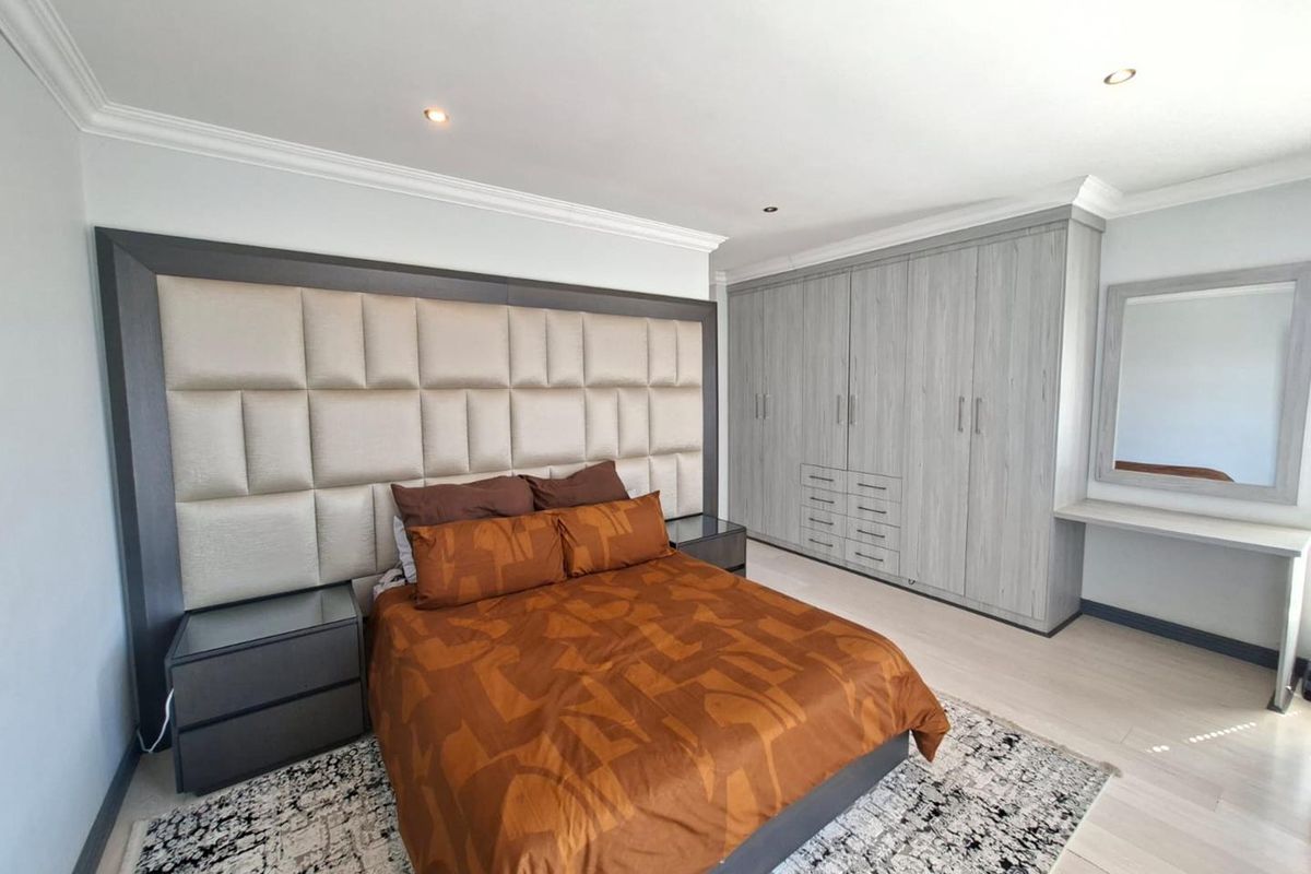 Spacious bedroom featuring extensive built-in cupboards, a dedicated vanity area, modern laminate flooring, and recessed downlighting.