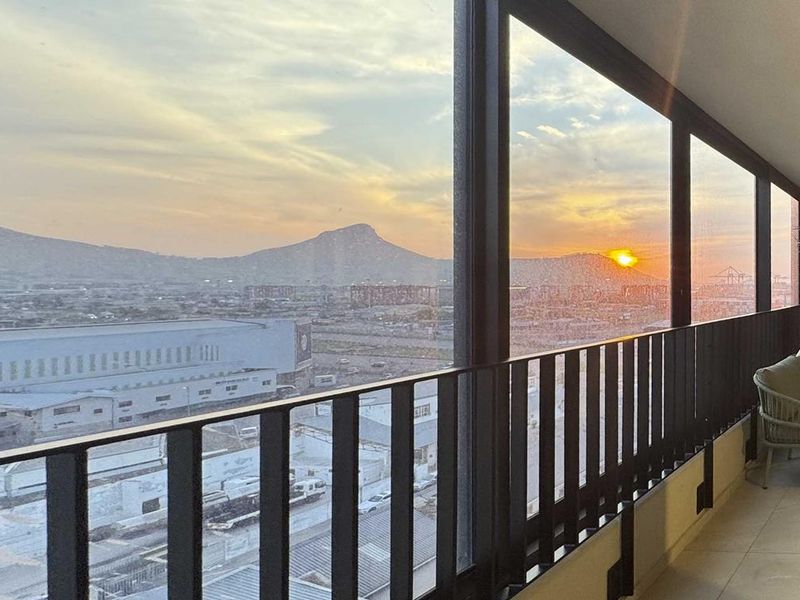 A modern covered balcony featuring tiled flooring, a sleek metal balustrade, and an exposed brick wall, offering expansive mountain and city views.