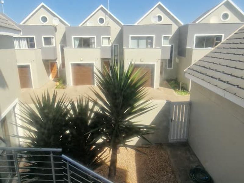 View of a modern townhouse complex rear courtyard featuring a tiled staircase with stainless steel balustrades and paved outdoor area.