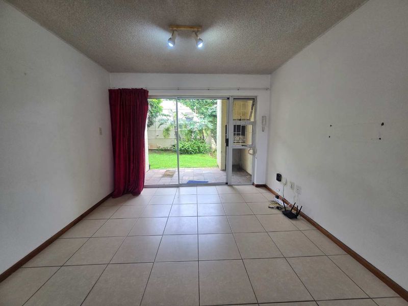 An empty living room featuring tiled flooring, a sliding glass door leading to a patio, and a ceiling-mounted spotlight fixture.