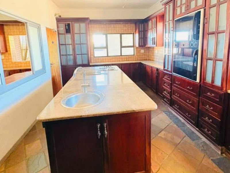 Spacious kitchen featuring a large central island with granite countertops, built-in oven, extensive wooden cabinetry, and durable tiled flooring.