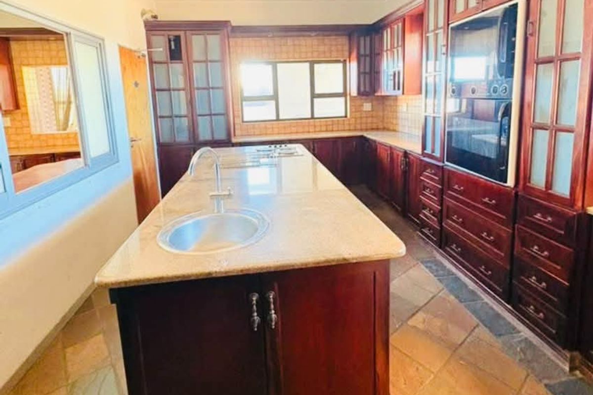 Spacious kitchen featuring a large central island with granite countertops, built-in oven, extensive wooden cabinetry, and durable tiled flooring.