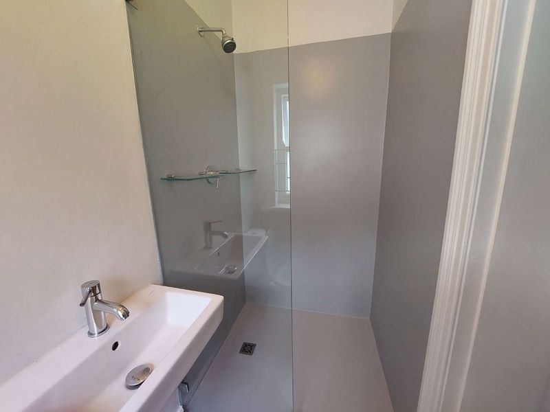 A modern, minimalist bathroom featuring a wall-mounted basin with chrome mixer tap and a spacious walk-in shower with a glass screen.
