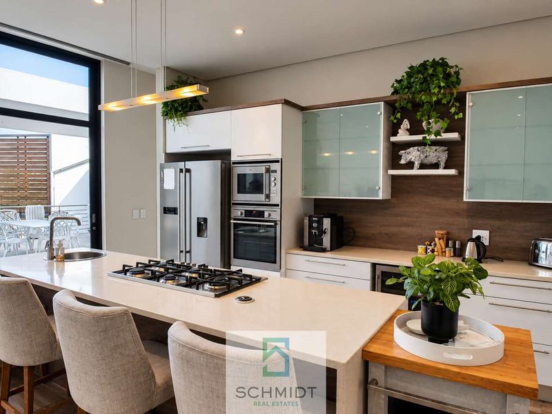 Modern kitchen featuring a large island with gas cooktop, stone countertops, built-in appliances, and sleek cabinetry, seamlessly connected to an outdoor patio area.