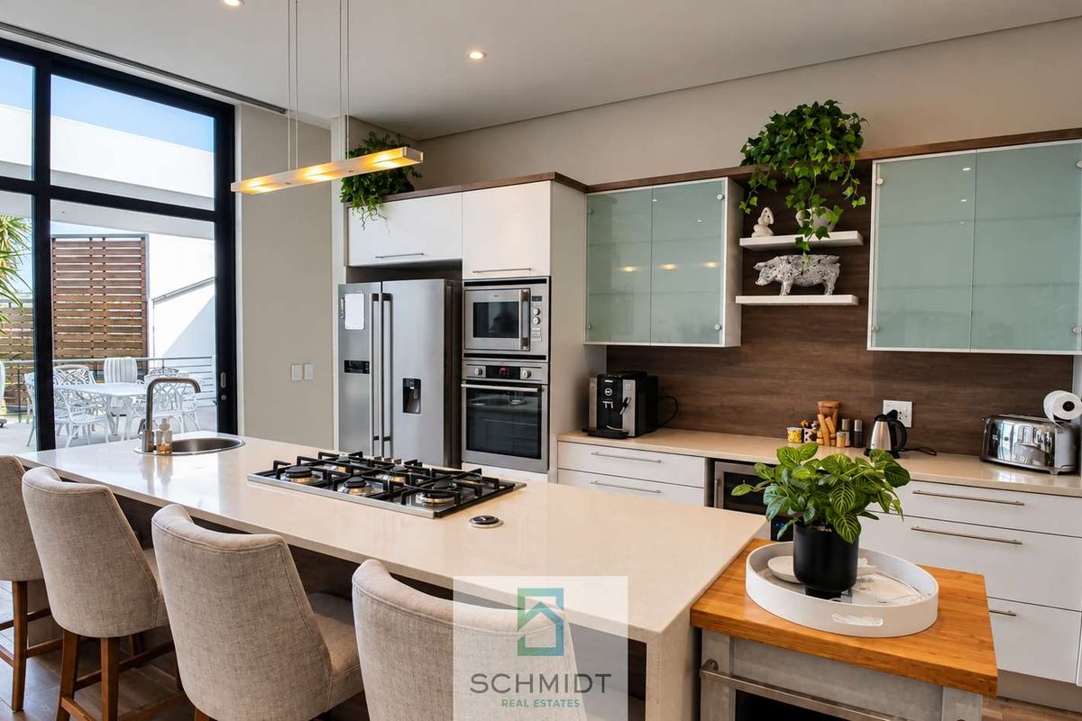Modern kitchen featuring a large island with gas cooktop, stone countertops, built-in appliances, and sleek cabinetry, seamlessly connected to an outdoor patio area.