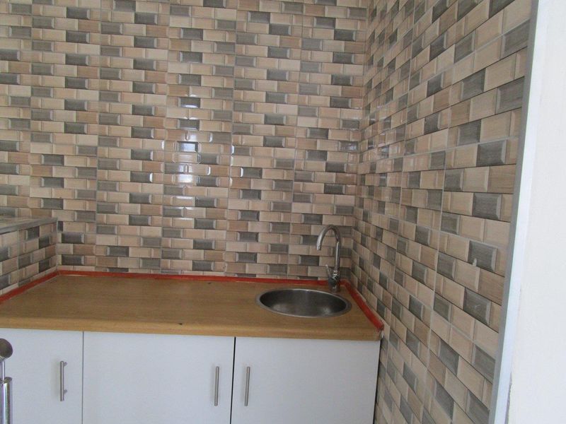 A compact kitchen area featuring white built-in cabinetry, a laminate countertop, and a stainless steel sink with tiled wall finishes.