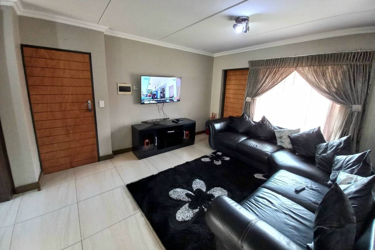 A comfortable living room featuring tiled flooring, neutral wall tones, and natural light through a window with draped curtains.
