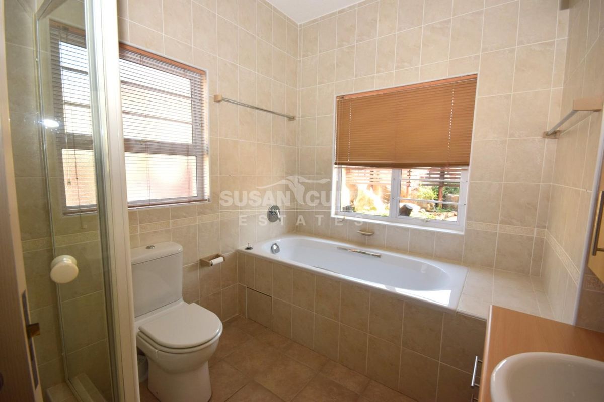 A functional bathroom featuring a built-in bathtub, separate shower enclosure, toilet, and vanity basin with neutral wall and floor tiling.