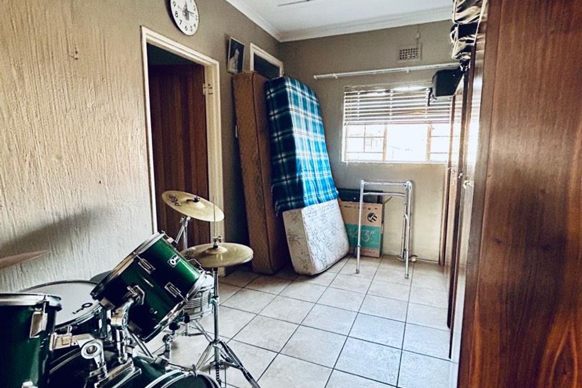A bedroom featuring tiled flooring, a window with blinds, and a ceiling access hatch, currently utilized as a multi-purpose storage and hobby space.
