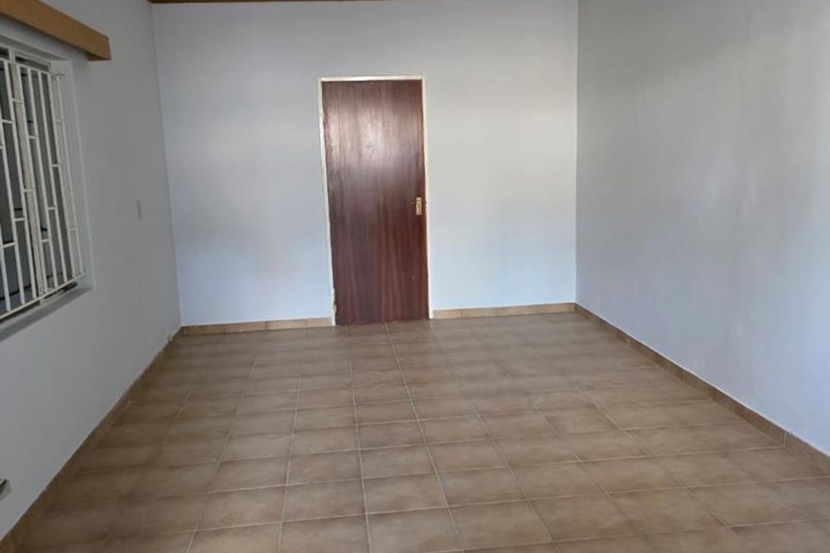 An empty living room featuring tiled flooring, a timber door, and security bars on the window, offering a blank canvas for renovation.