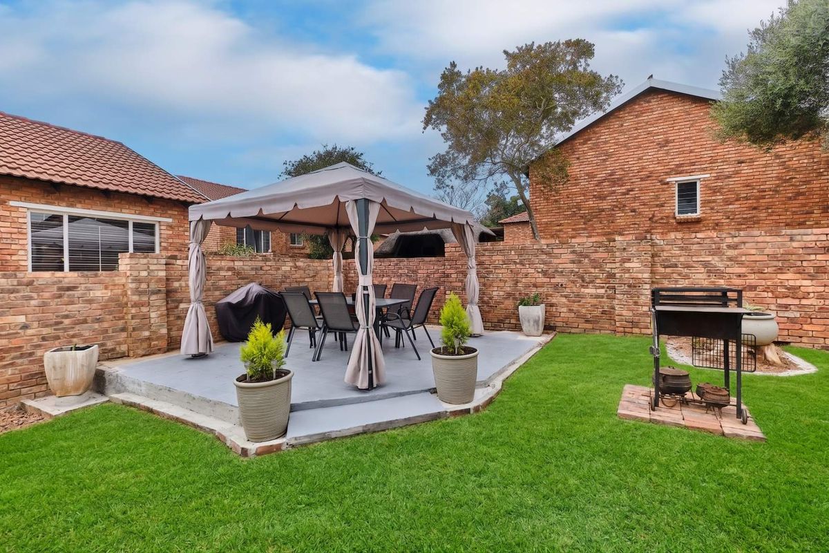 A private rear garden featuring a paved patio area, brick boundary walls, and a dedicated outdoor braai space with a lawn.