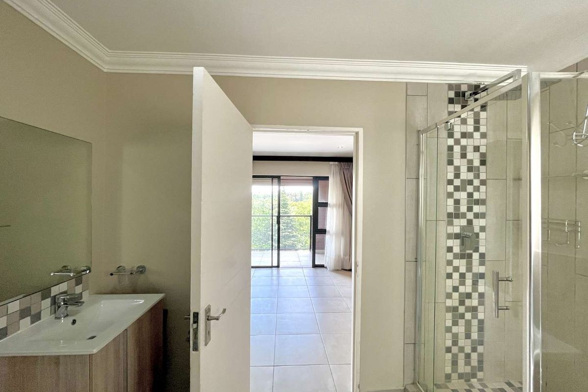A well-maintained bathroom featuring a vanity with basin, a glass-enclosed shower with decorative mosaic tiling, and direct access to an adjacent living area.
