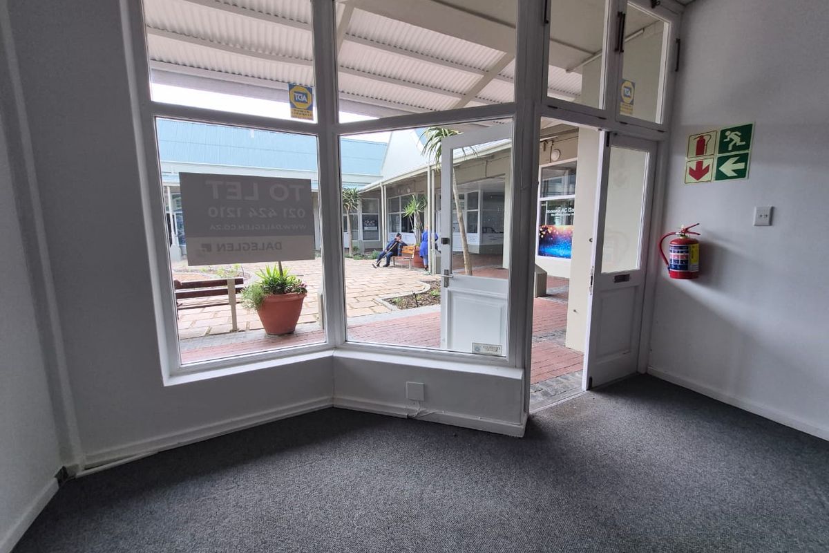 A bright, empty retail entrance space featuring large display windows, carpeted flooring, and direct access to an outdoor courtyard area.