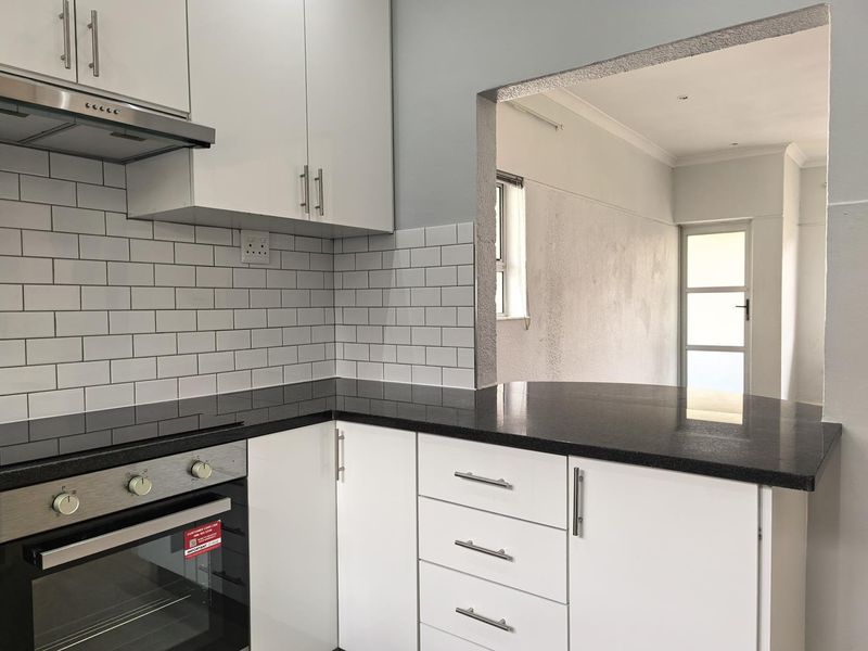 Modern kitchen featuring white cabinetry, black granite countertops, subway tile backsplash, and a convenient pass-through window connecting to the adjacent living area.