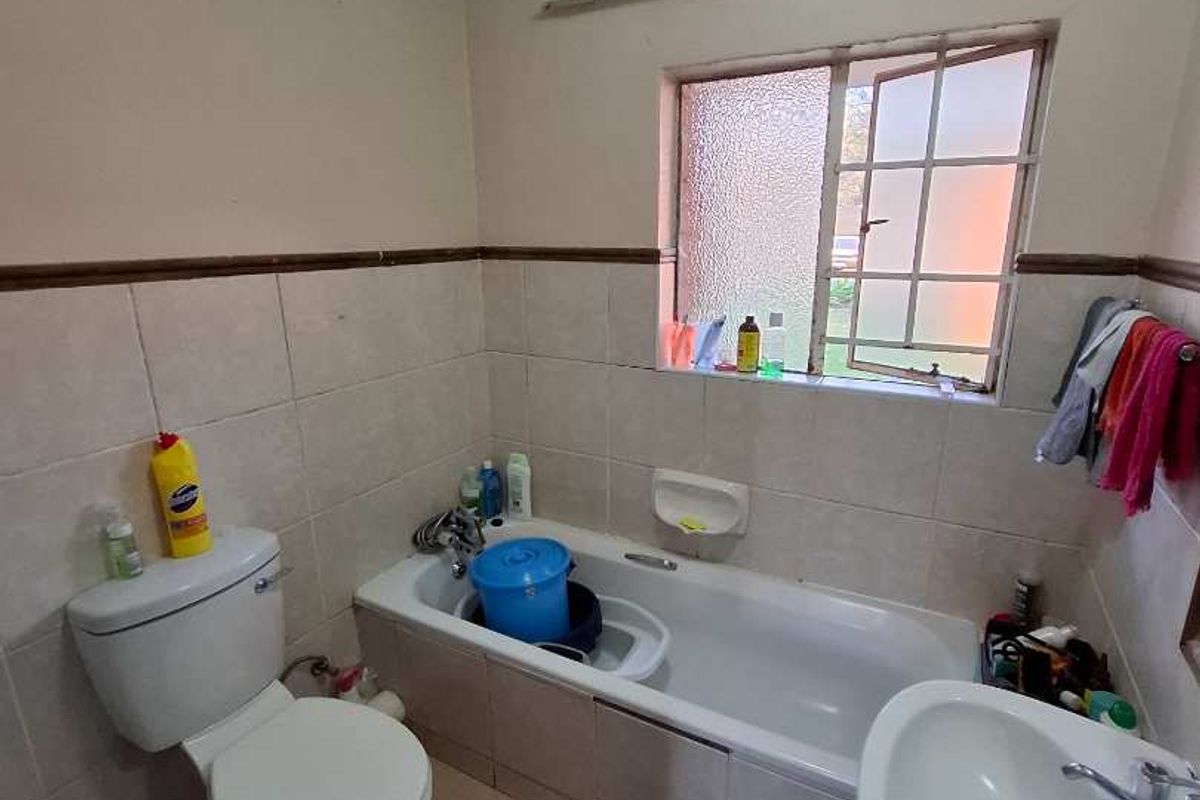A dated bathroom featuring a standard bathtub, pedestal basin, and toilet, with tiled finishes and a window for natural light.